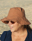 lady at the beach wearing a clay coloured cotton bucket hat. great sun protection. wide brim that stays in place due to wire in the rim