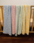 cotton baby blankets in four colours displayed on a cot