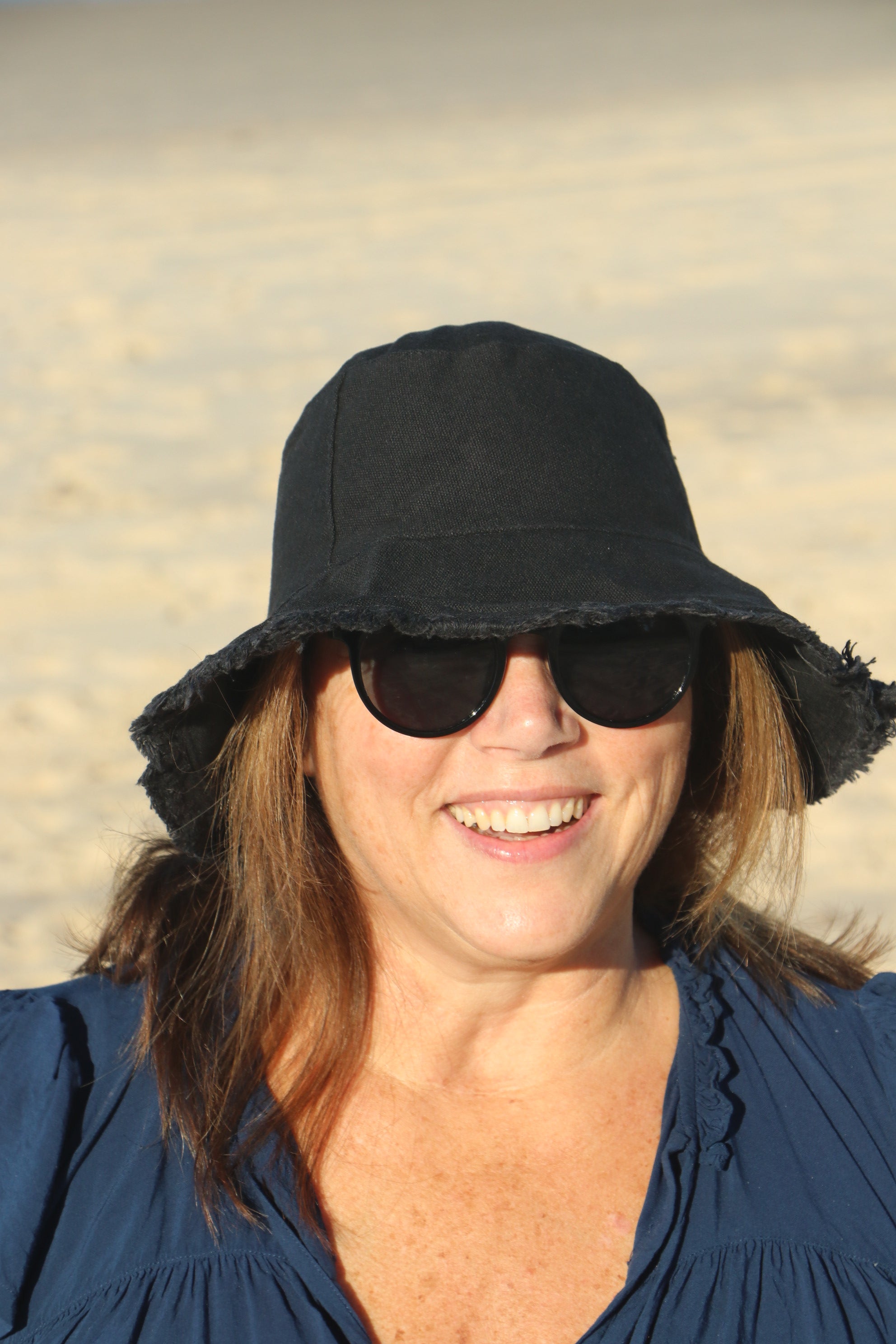 smiling lady on beach wearing a black hat and sunglasses