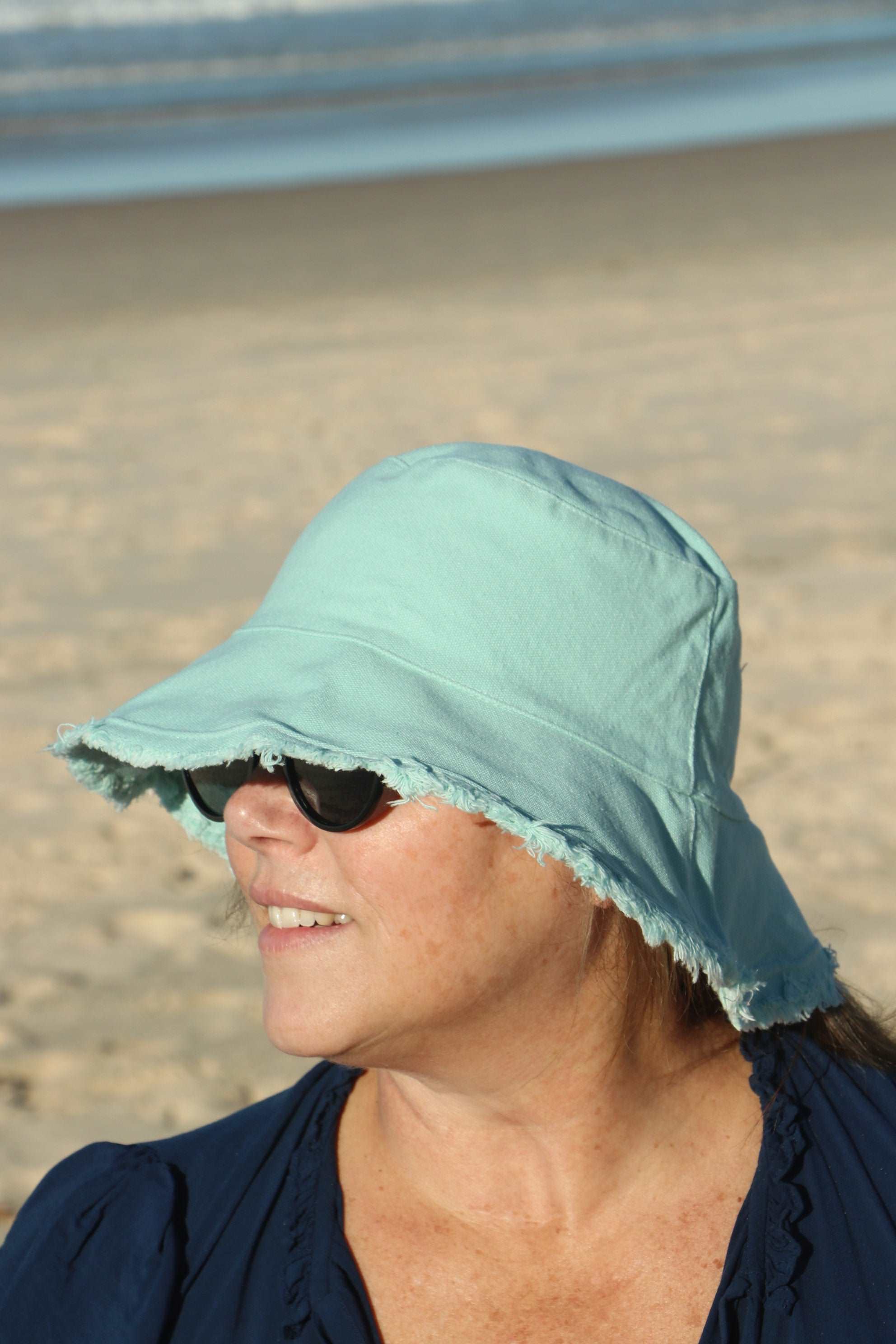lady at the beach wearing a mint green coloured cotton bucket hat. great sun protection. wide brim that stays in place due to wire in the rim