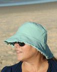 lady at the beach wearing a mint green coloured cotton bucket hat. great sun protection. wide brim that stays in place due to wire in the rim