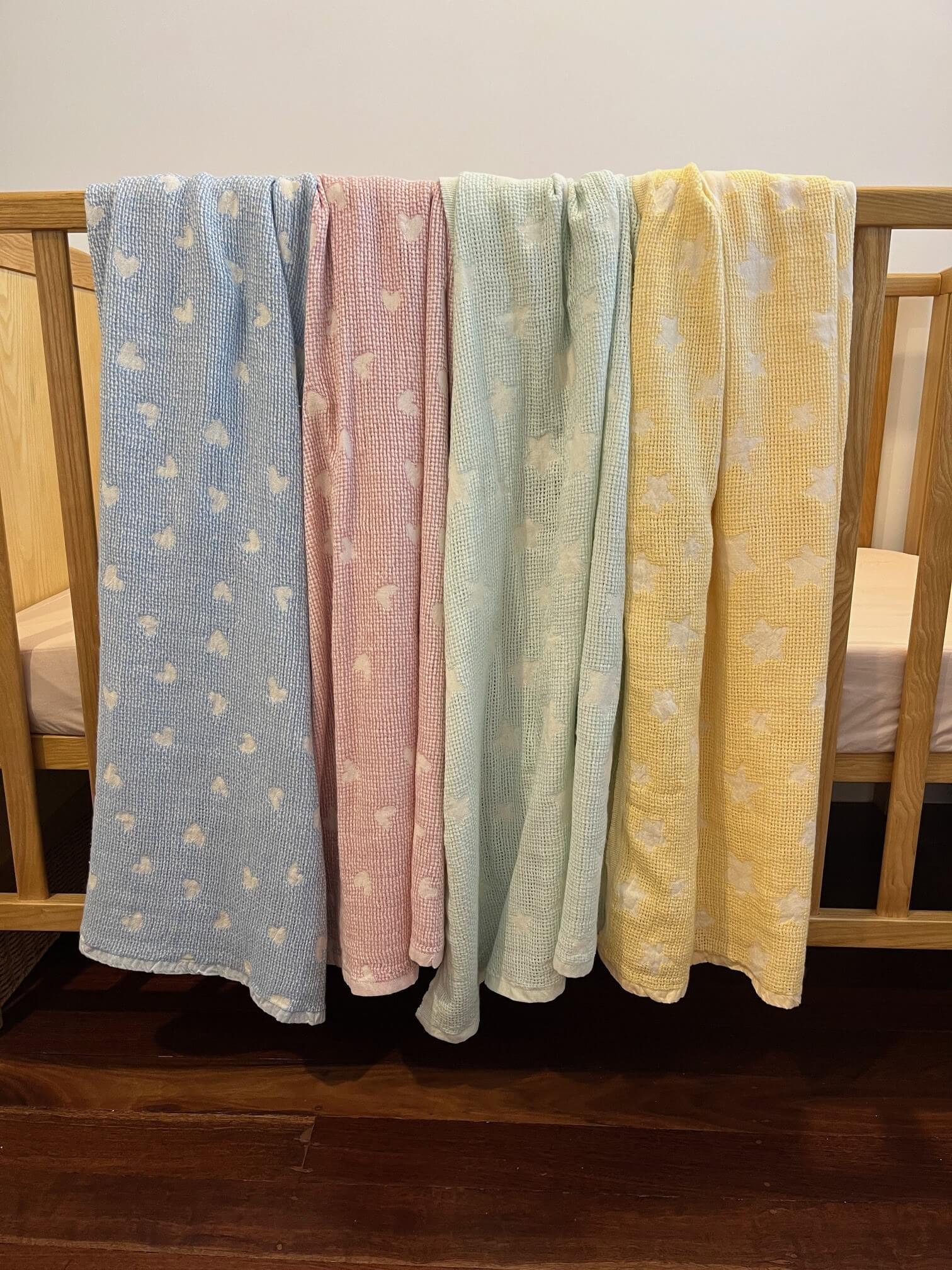 cotton baby blankets in four colours displayed on a cot